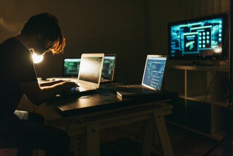 person with multiple computers in a dark room